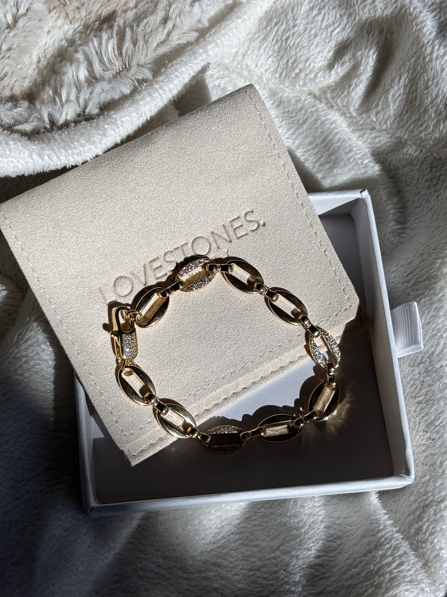 Gold chain bracelet in a branded jewelry box on a soft fabric background