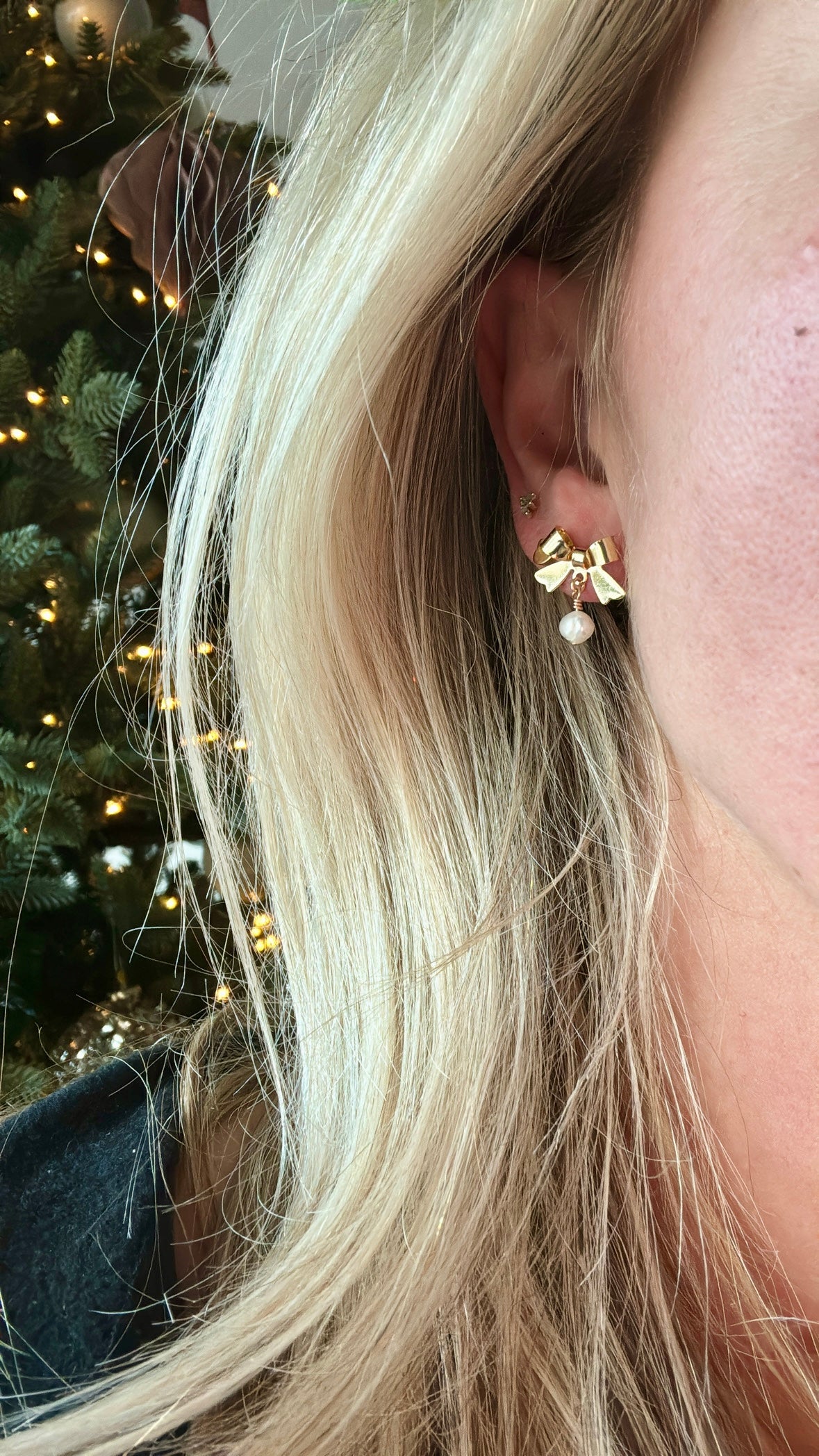 bow and pearl earrings on model with christmas tree behind