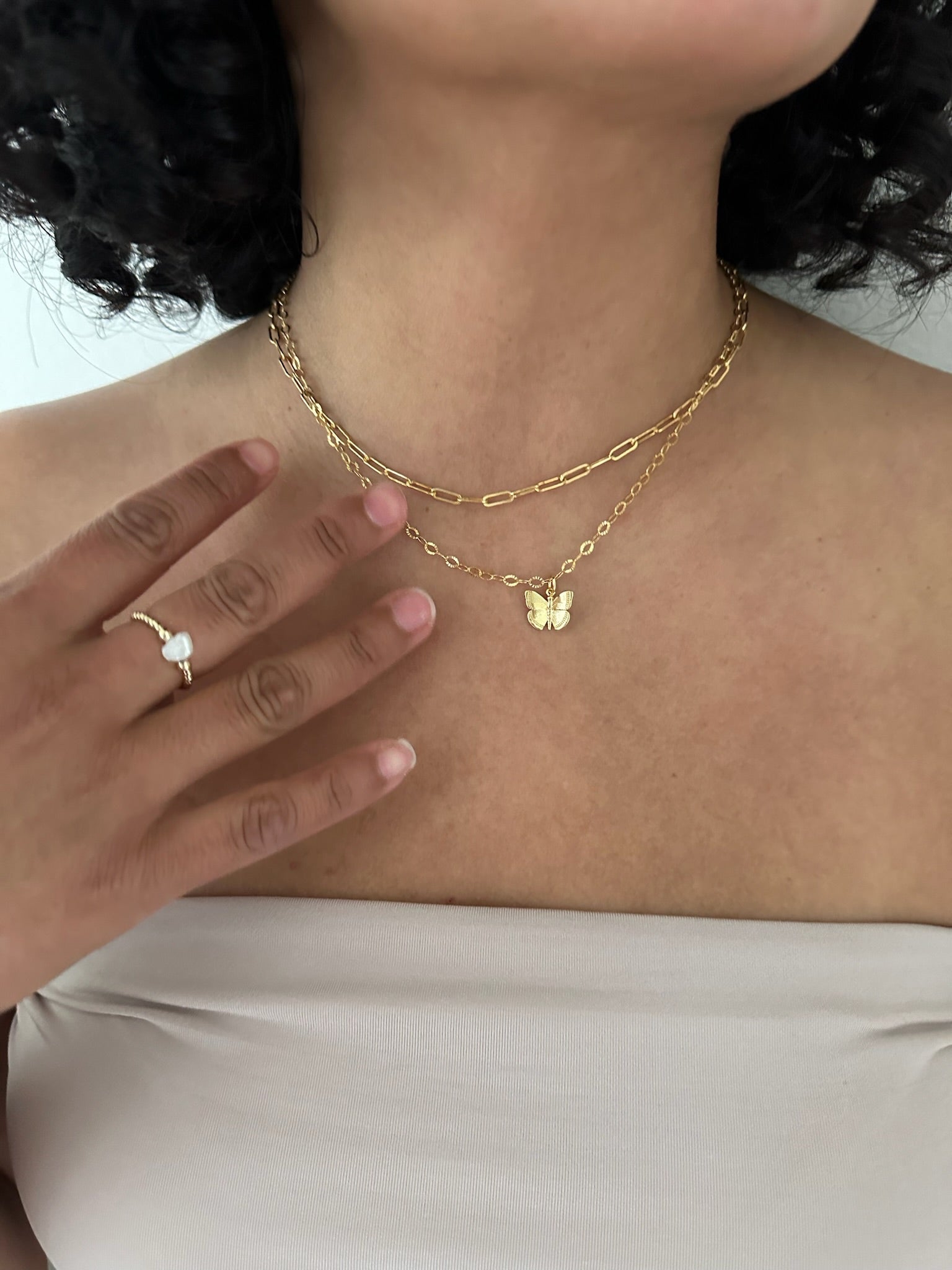 Model wearing a gold paperclip necklace and mariposa gold chain butterfly necklace. 