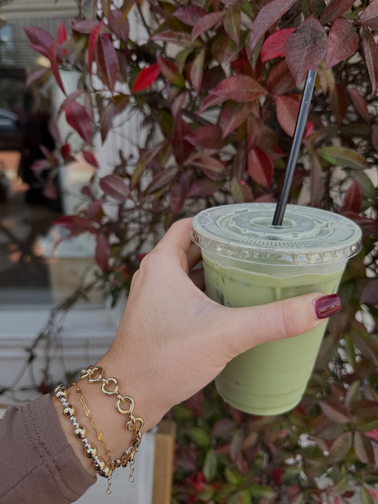 model wearing bracelets holding a matcha in front of leaves